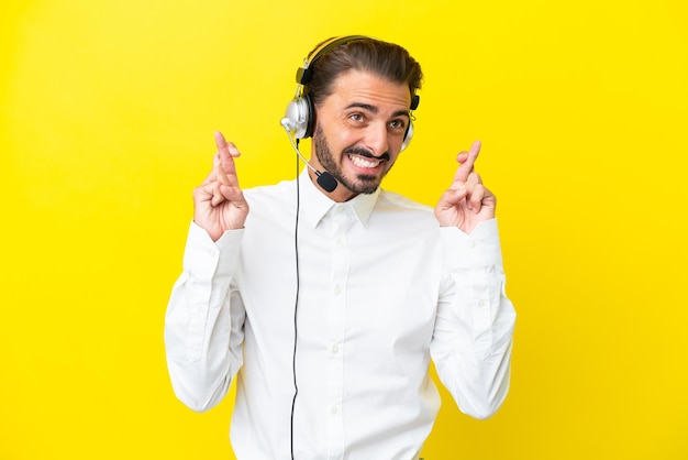 Telemarketeer blanke man aan het werk met een headset geïsoleerd op gele achtergrond met vingers over elkaar