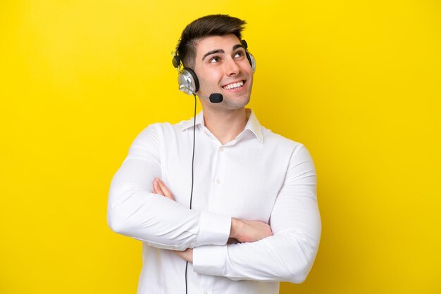 Telemarketeer blanke man aan het werk met een headset geïsoleerd op gele achtergrond terwijl hij glimlacht