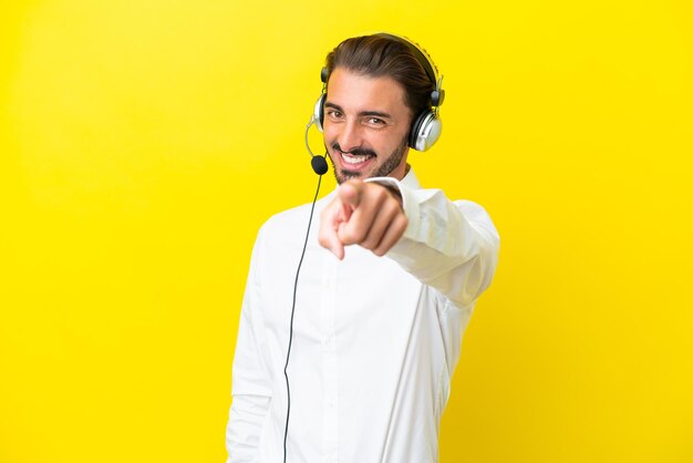 Telemarketeer blanke man aan het werk met een headset geïsoleerd op gele achtergrond wijst vinger naar je met een zelfverzekerde uitdrukking