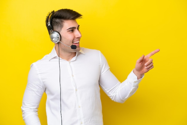 Telemarketeer blanke man aan het werk met een headset geïsoleerd op gele achtergrond wijzende vinger naar de zijkant en presenteren van een product