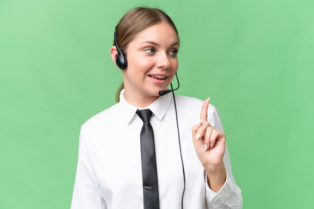 Telemarketeer blanke vrouw die met een headset over een geïsoleerde achtergrond werkt en de oplossing wil realiseren terwijl ze een vinger opsteekt