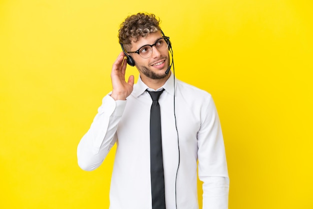 Telemarketeer blonde man aan het werk met een headset geïsoleerd op gele achtergrond denken een idee