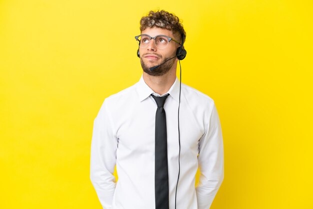 Telemarketeer blonde man aan het werk met een headset geïsoleerd op gele achtergrond en opzoeken