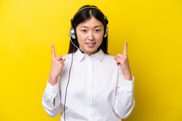 Telemarketeer Chinese vrouw die werkt met een headset geïsoleerd op een gele achtergrond die een geweldig idee benadrukt