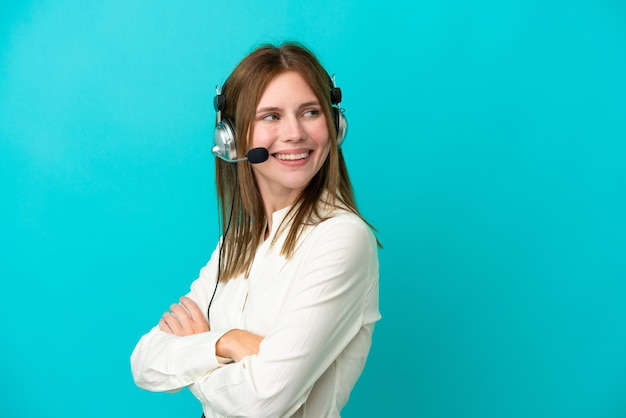 Telemarketeer Engelse vrouw die werkt met een headset geïsoleerd op een blauwe achtergrond met gekruiste armen en blij