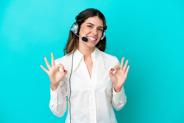 Telemarketeer Italiaanse vrouw die werkt met een headset geïsoleerd op een blauwe achtergrond met een ok-teken met vingers