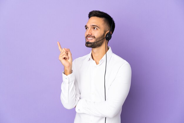 Telemarketeer man aan het werk met een headset geïsoleerd op paarse muur met een geweldig idee