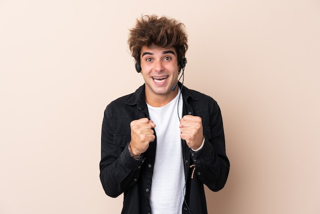 Telemarketeer man aan het werk met een headset over geïsoleerde muur een overwinning vieren