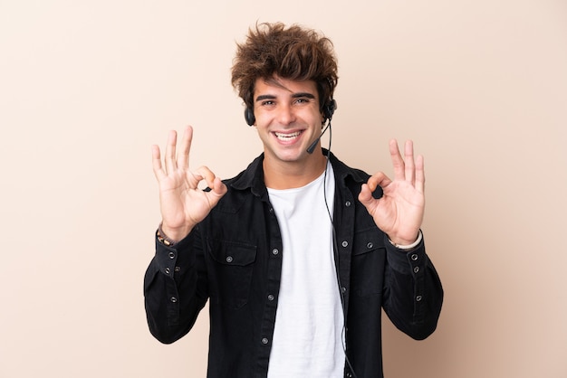 Telemarketeer man aan het werk met een headset over geïsoleerde muur met een ok bord met vingers