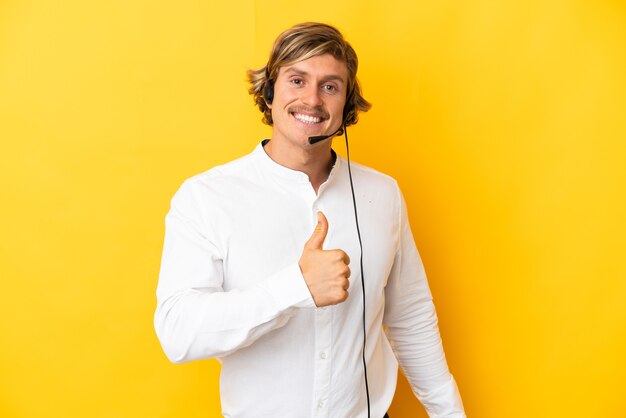 Telemarketeer man aan het werk met een hoofdtelefoon geïsoleerd op gele muur met een duim omhoog gebaar