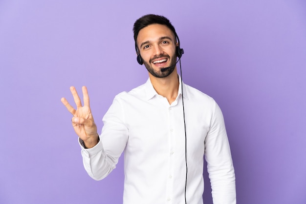 Telemarketeer man aan het werk met een hoofdtelefoon geïsoleerd op paarse achtergrond gelukkig en drie met vingers tellen