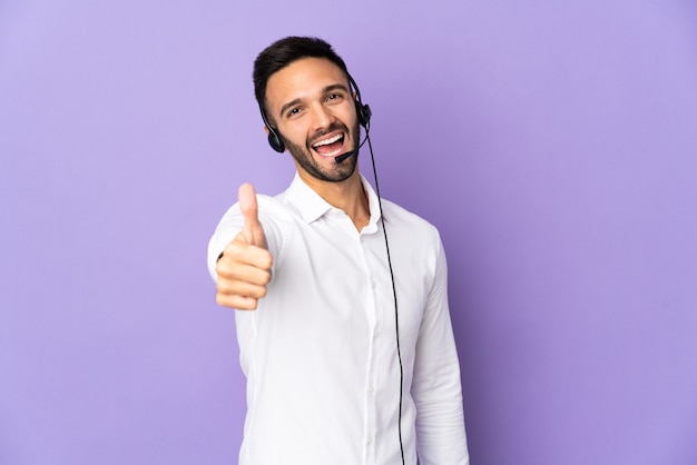 Telemarketeer man aan het werk met een hoofdtelefoon geïsoleerd op paarse muur met duimen omhoog omdat er iets goeds is gebeurd