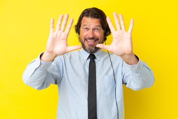 Telemarketeer Nederlandse man aan het werk met een headset geïsoleerd op een gele achtergrond die tien telt met vingers