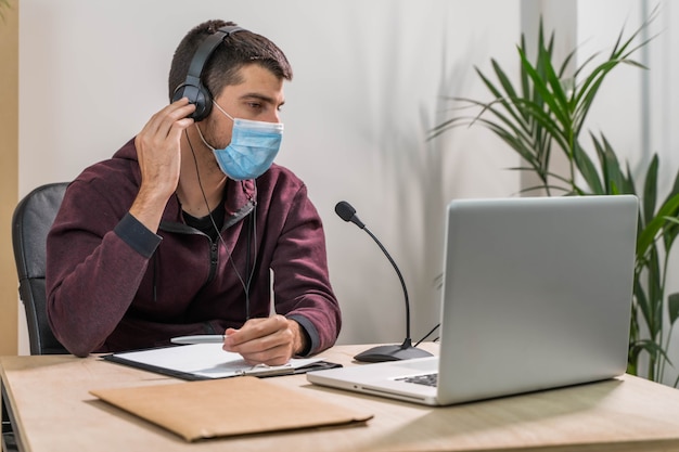 Telemarketeer of podcast man aan het werk met laptop en praten op een headset met gezichtsmasker op kantoor