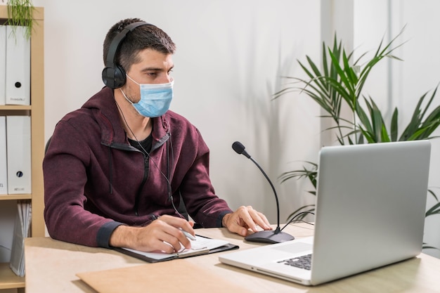 Telemarketeer of podcast man aan het werk met laptop en praten op een headset met gezichtsmasker op kantoor