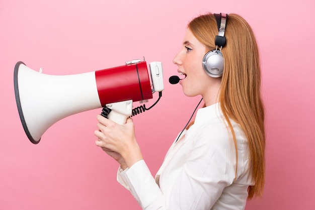 Telemarketeer roodharige vrouw die werkt met een headset geïsoleerd op roze achtergrond schreeuwen door een megafoon