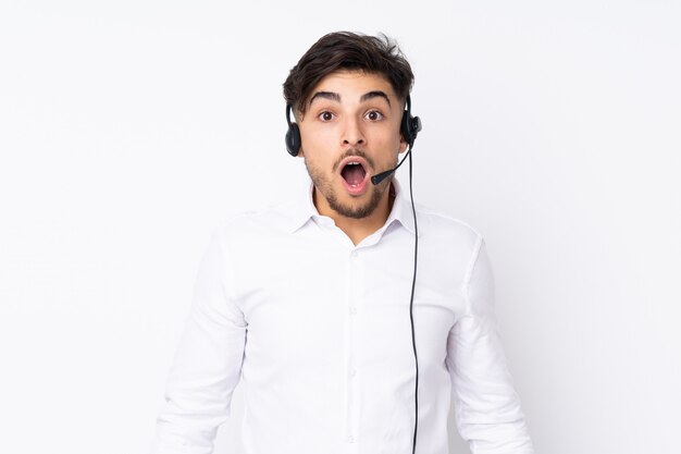 Telemarketer Arabian man working with a headset on white wall with surprised facial expression