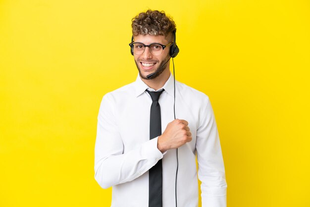 Telemarketer blonde man working with a headset isolated on yellow background celebrating a victory