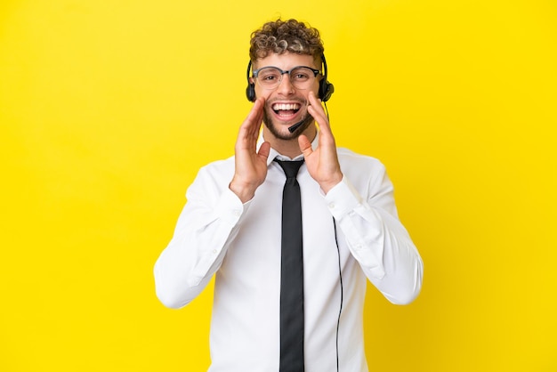 Telemarketer blonde man working with a headset isolated on yellow background shouting and announcing something