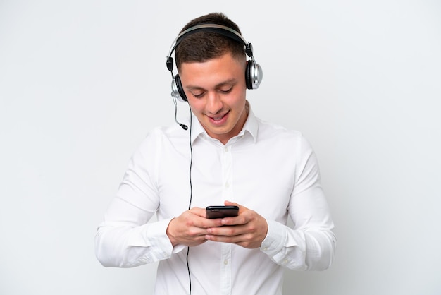 Telemarketer Brazilian man working with a headset isolated on white background sending a message with the mobile