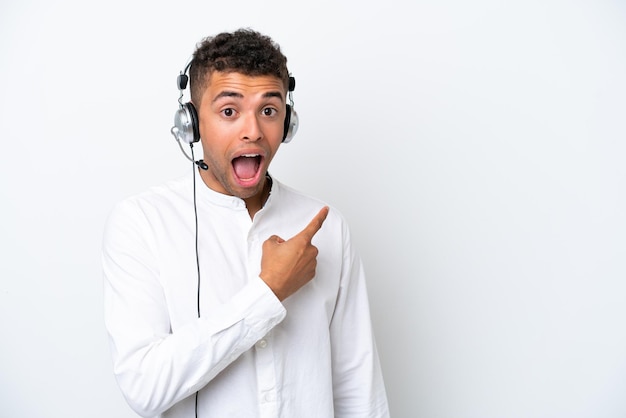 Telemarketer Brazilian man working with a headset isolated on white background surprised and pointing side