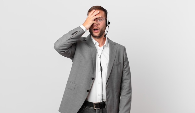 Telemarketer businessman looking shocked, scared or terrified, covering face with hand