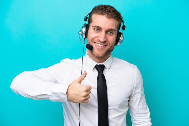 Foto telemarketer uomo caucasico che lavora con un auricolare isolato su sfondo blu dando un pollice in alto gesto