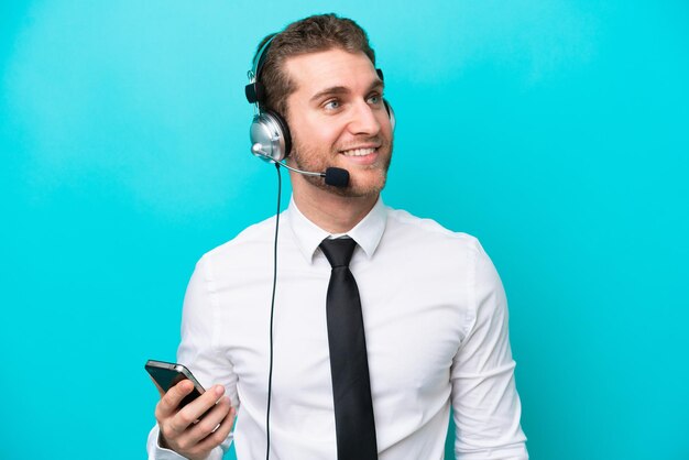 Telemarketer uomo caucasico che lavora con un auricolare isolato su sfondo blu mantenendo una conversazione con il telefono cellulare