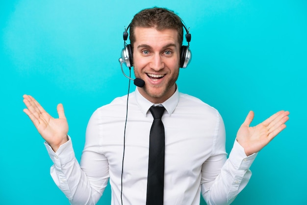 Telemarketer caucasian man working with a headset isolated on blue background with shocked facial expression