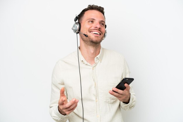 Telemarketer caucasian man working with a headset isolated on white background keeping a conversation with the mobile phone with someone