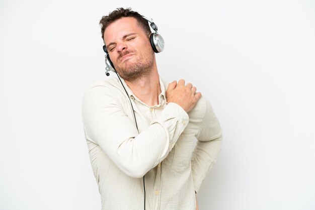 Telemarketer caucasian man working with a headset isolated on white background suffering from pain in shoulder for having made an effort