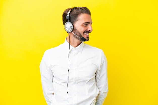 Telemarketer caucasian man working with a headset isolated on yellow background looking side