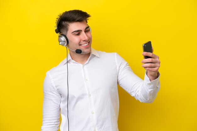 Telemarketer uomo caucasico che lavora con un auricolare isolato su sfondo giallo facendo un selfie