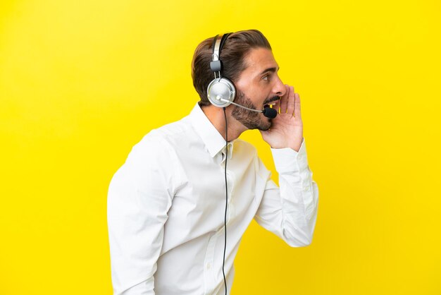 Telemarketer caucasian man working with a headset isolated on yellow background shouting with mouth wide open to the lateral