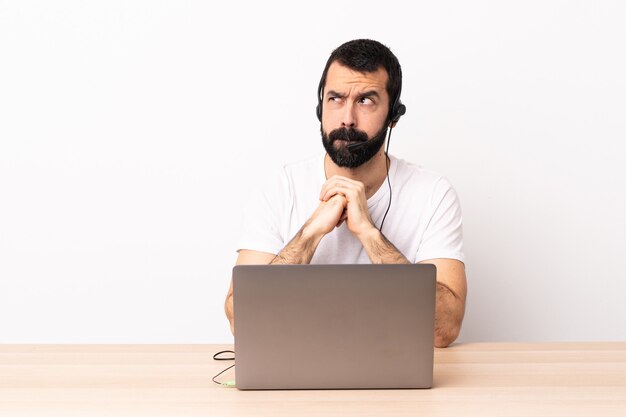 Telemarketer caucasian man working with a headset and with laptop having doubts while looking up.