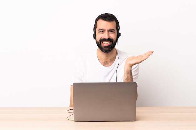 Telemarketer caucasian man working with a headset and with laptop holding copyspace imaginary on the palm to insert an ad.
