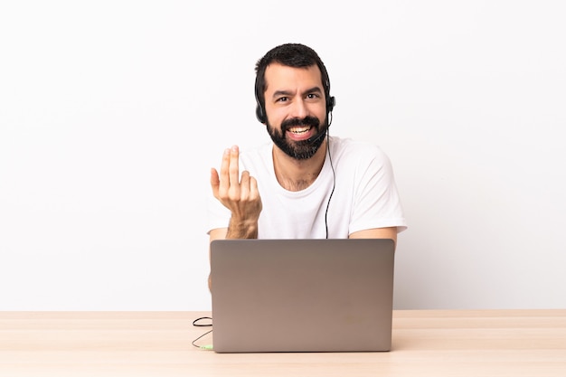 Telemarketer caucasian man working with a headset and with laptop inviting to come with hand. Happy that you came