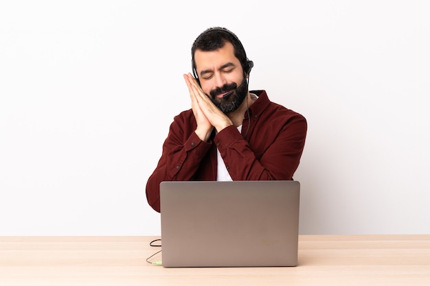 Telemarketer caucasian man working with a headset and with laptop making sleep gesture in dorable expression.