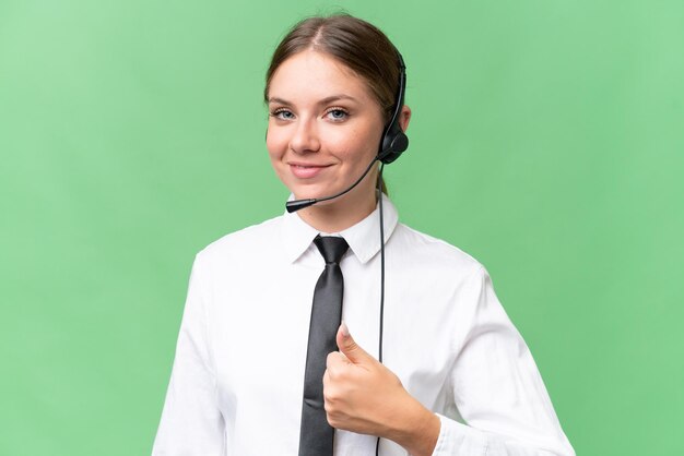 Telemarketer caucasian woman working with a headset over isolated background with thumbs up because something good has happened