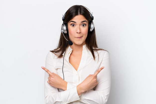 Telemarketer caucasian woman working with a headset isolated on white background pointing to the laterals having doubts