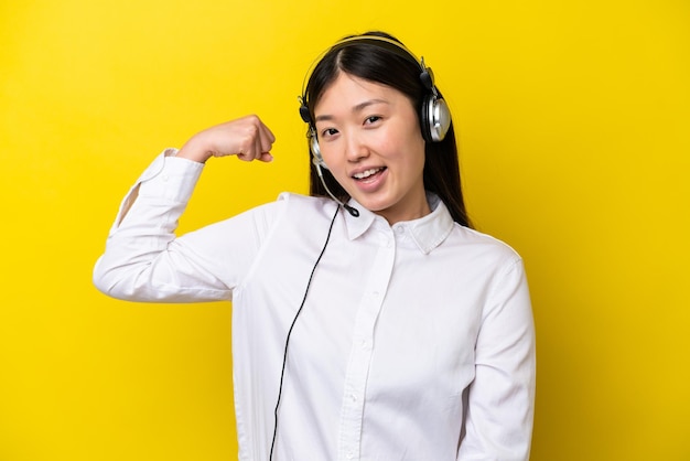 Telemarketer Chinese woman working with a headset isolated on yellow background doing strong gesture