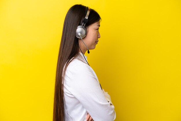 Telemarketer donna cinese che lavora con un auricolare isolato su sfondo giallo in posizione laterale