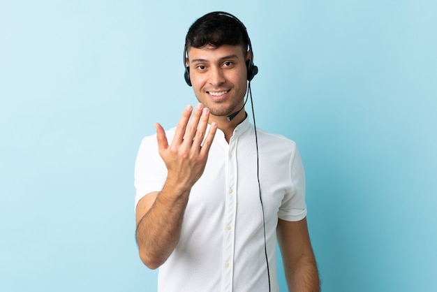 Operatore di telemarketer colombiano uomo che lavora con un auricolare isolato invitando a venire con la mano. felice che tu sia venuto