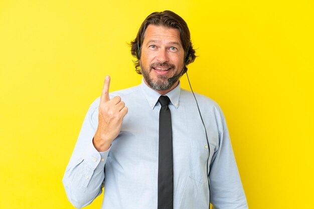 Голландский телемаркетер, работающий с гарнитурой, изолирован на желтом фоне, указывая указательным пальцем - отличная идея