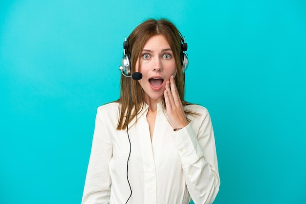 Telemarketer English woman working with a headset isolated on blue background with surprise and shocked facial expression