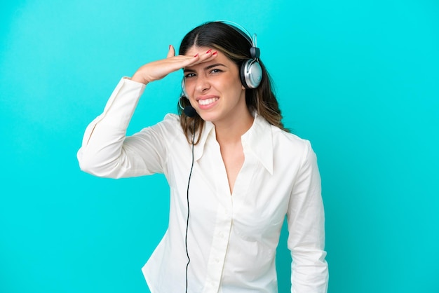 Telemarketer Italian woman working with a headset isolated on blue background looking far away with hand to look something