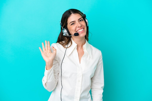 Telemarketer donna italiana che lavora con un auricolare isolato su sfondo blu salutando con la mano con espressione felice