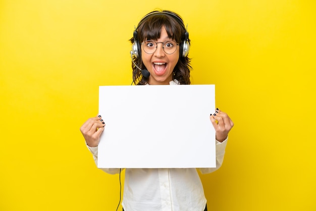 Telemarketer latin woman working with a headset isolated on yellow background holding an empty placard with happy expression