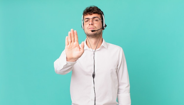 Telemarketer dall'aspetto serio, severo, dispiaciuto e arrabbiato che mostra il palmo aperto che fa un gesto di arresto