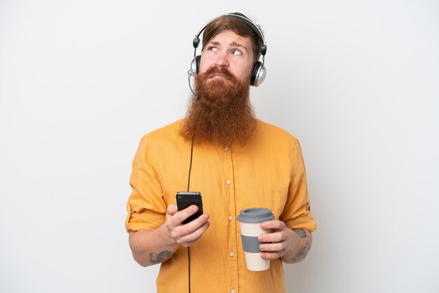 흰색 배경에 격리된 텔레마케터 남자는 커피를 들고 무언가를 생각하는 동안 휴대전화를 들고 있습니다.